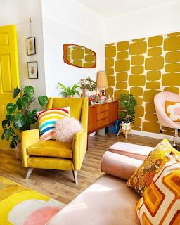Colorful retro living room with yellow armchair, patterned wallpaper, plants, and mid-century furniture