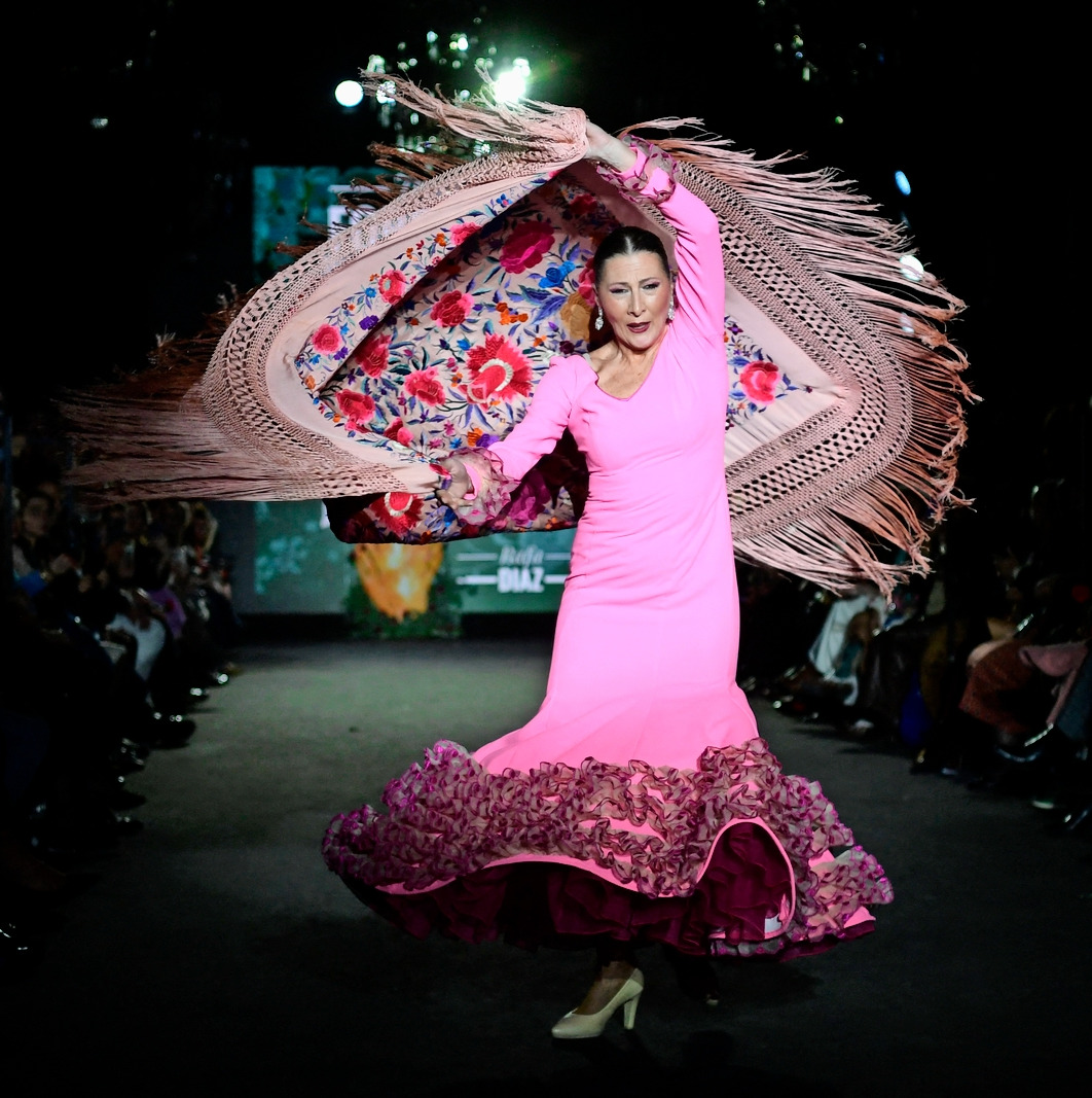 Woman in a pink flamenco dress holding a fringed floral shawl on a fashion runway