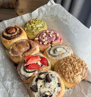 Assorted iced sweet rolls on parchment paper with toppings like strawberries, cookies, nuts, and pistachios