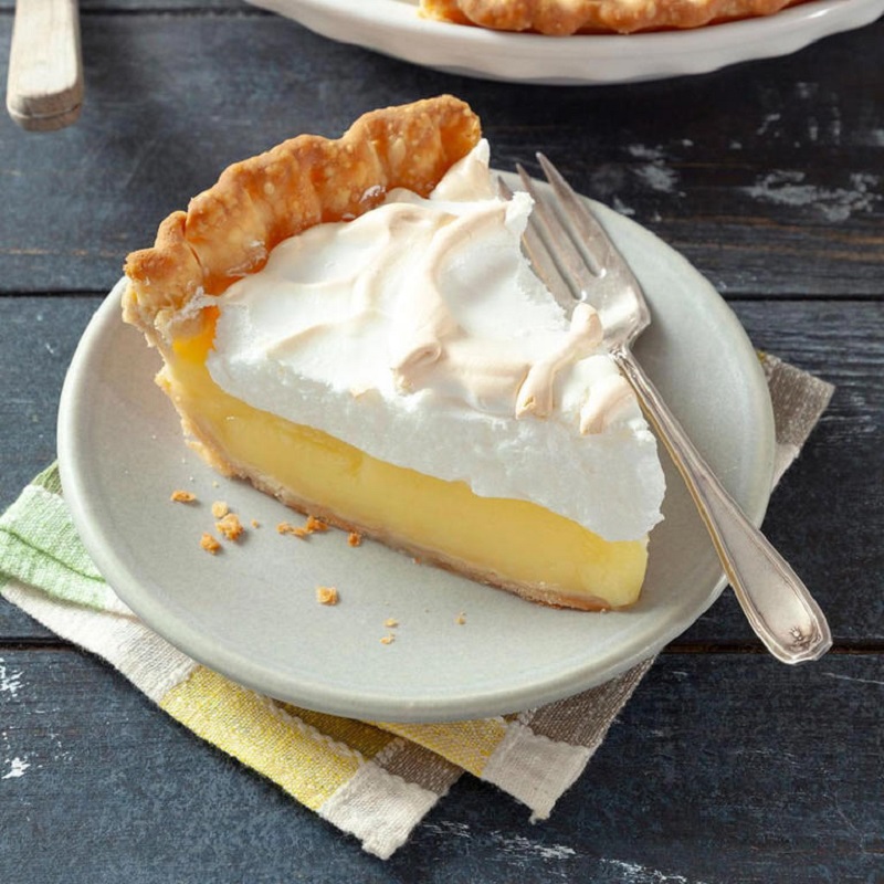 Slice of lemon meringue pie with toasted meringue on white plate with fork