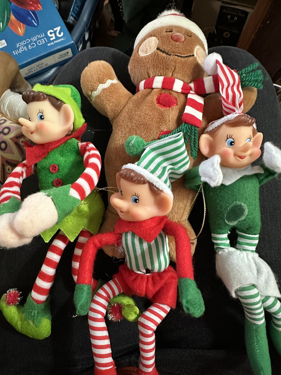 Three Christmas elf dolls and a gingerbread plush sitting on a dark chair