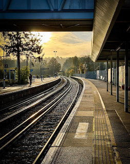 Curved railway tracks at a train station platform during golden sunset with trees in the background