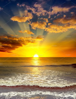 Golden sunrise over ocean with dramatic clouds and waves breaking on sandy beach