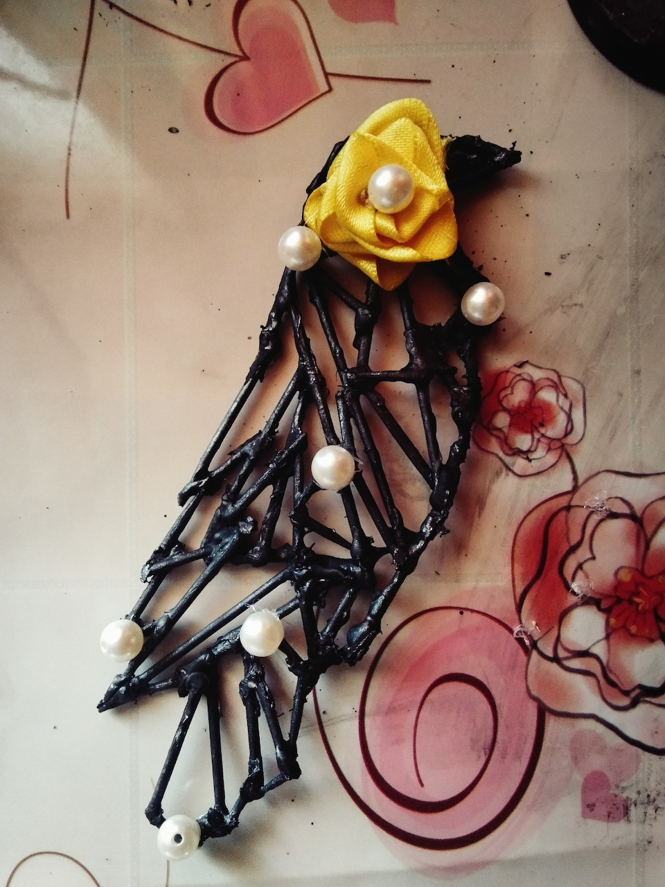 Black wire brooch with yellow rose and pearl beads on patterned fabric