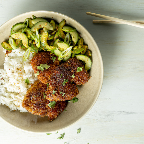 Crispy Korean fried chicken with rice and cucumber salad on a white plate