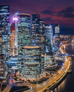 Aerial night view of illuminated Moscow City skyscrapers against purple-orange sky with highway light trails