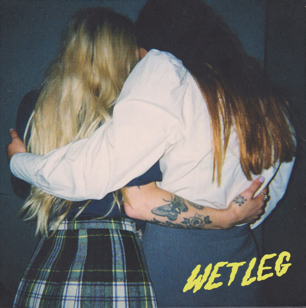 Two women in white shirts and plaid skirts embracing with their heads together, obscuring their faces