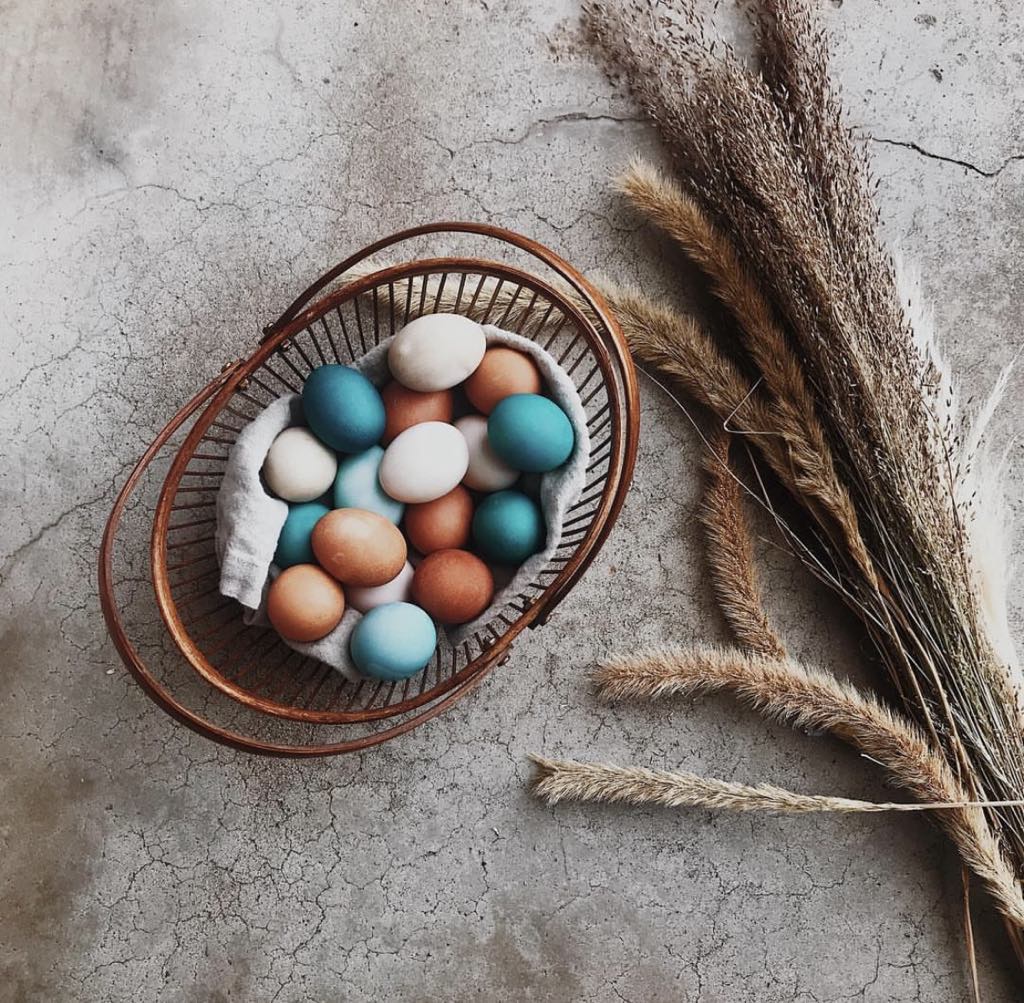 Pastel Easter eggs in a wicker basket beside dried grass on a rustic surface