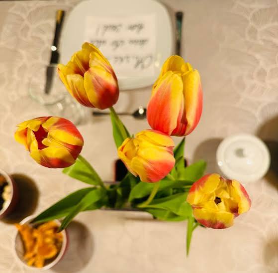 Overhead view of yellow and red tulips in a vase on a table with a teacup and small dishes