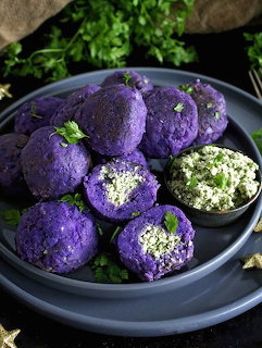 Purple sweet potato balls on a dark plate with herb filling and parsley garnish