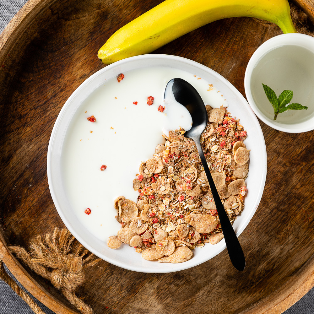 Bowl of muesli and yogurt with banana and tea on wooden tray