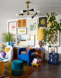 Bright living room corner with blue chair, artwork gallery wall, plants, and colorful decorative accents