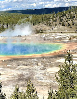 Colorful hot spring with blue center, orange edges, steam and forest