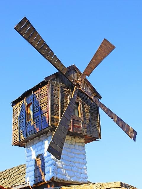 Old wooden windmill with four blades against blue sky