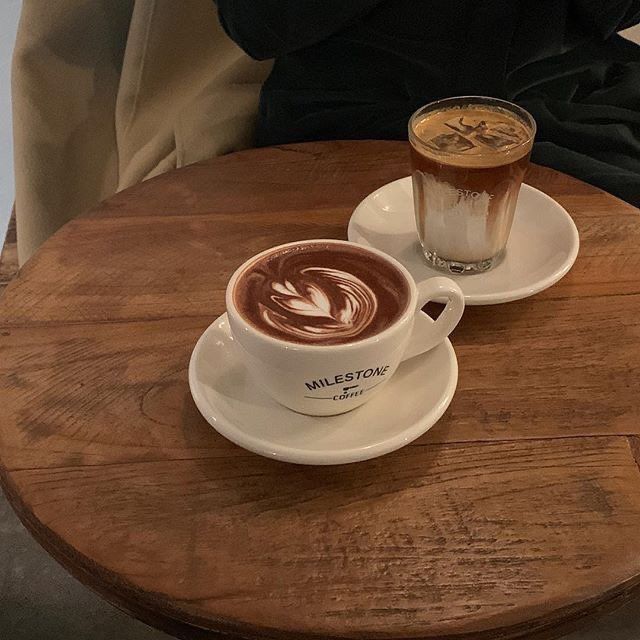Latte with leaf art and a layered iced coffee on a round wooden table