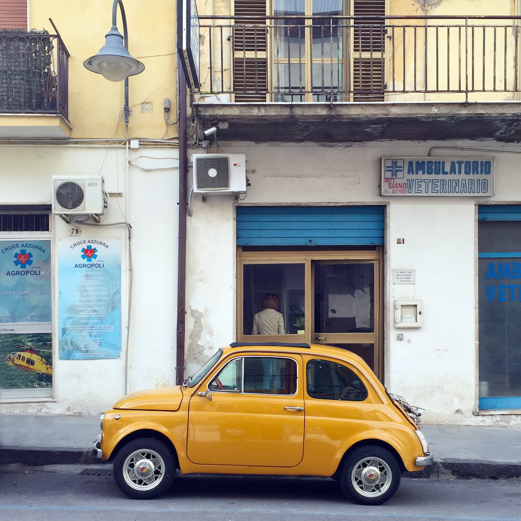 Yellow vintage Fiat 500 parked on urban street beside white building