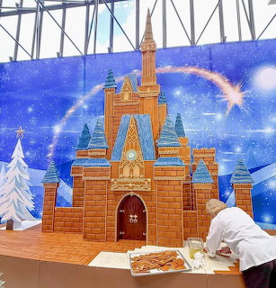 Large gingerbread castle with Disney-style architecture displayed under starry blue backdrop with rainbow