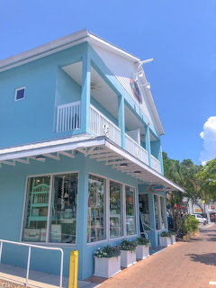 Turquoise two-story coastal building with white balcony and large shop windows under blue sky