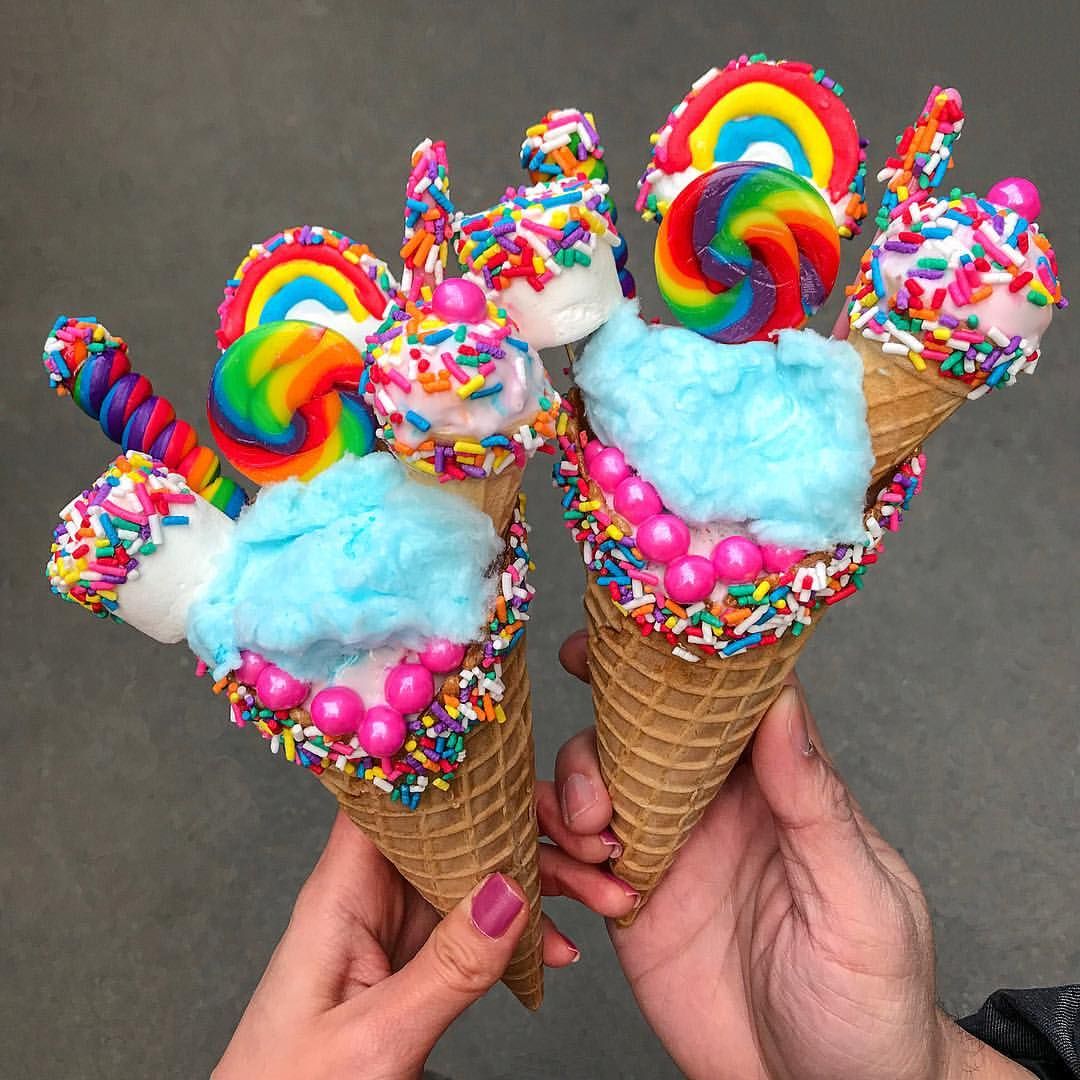 Hands holding vibrant rainbow ice cream cones decorated with colorful sprinkles and lollipops