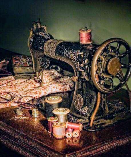 Ornate vintage black sewing machine with gold decorative patterns on wooden table with thread spools and lace