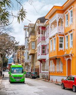 Colorful historic houses along a narrow city street with parked cars and a green bus