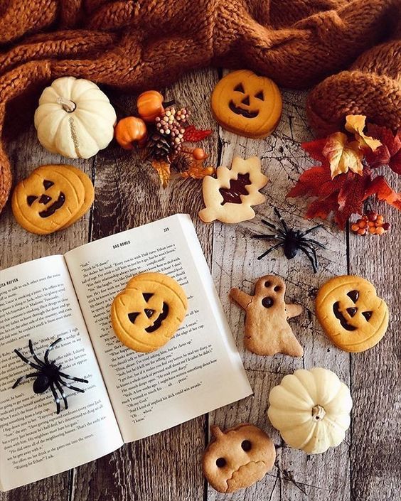 Halloween cookies decorated as jack-o-lanterns with pumpkins, autumn leaves, and spiders on wooden surface