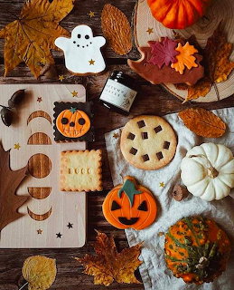 Halloween cookies with ghost, pumpkin, and fall leaf designs on wooden board with autumn decor