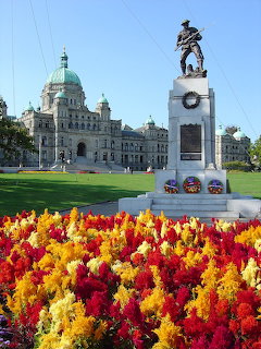 BC Parliament Buildings in Victoria with war memorial statue and colorful red and yellow flowers in foreground