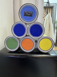 Six open paint cans stacked in a pyramid showing blue, green, orange, and yellow paint