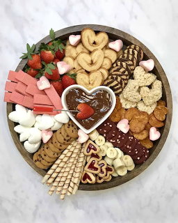 Circular charcuterie board with crackers, meats, cheese, strawberries, and heart-shaped dip bowl on marble surface