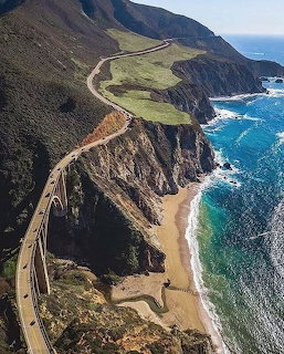 Winding Highway 1 along steep coastal cliffs above a sandy beach and blue ocean