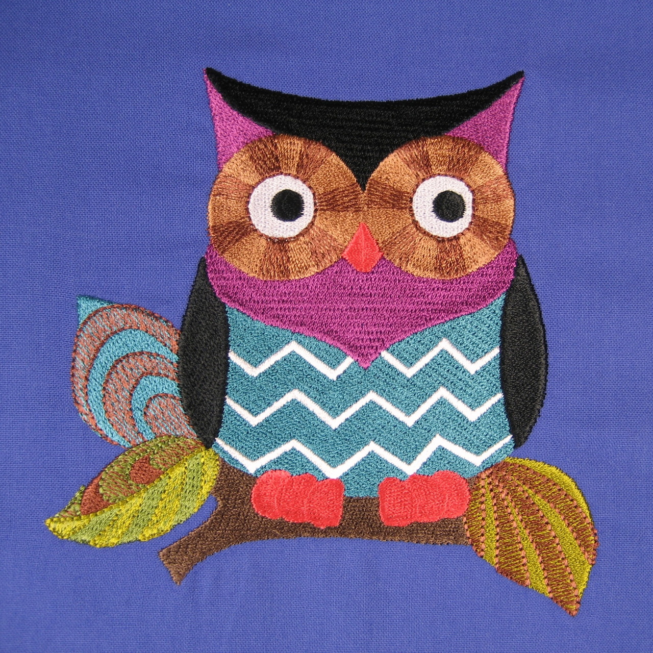 Colorful embroidered owl with chevron pattern and button eyes on blue fabric background