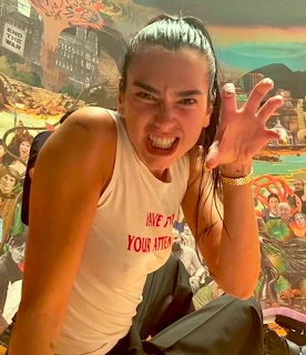 Woman making a playful fierce face with raised hand in front of a colorful mural