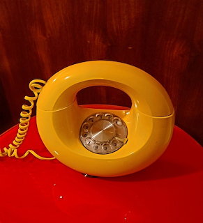 Yellow rotary telephone on a red table with a wood background