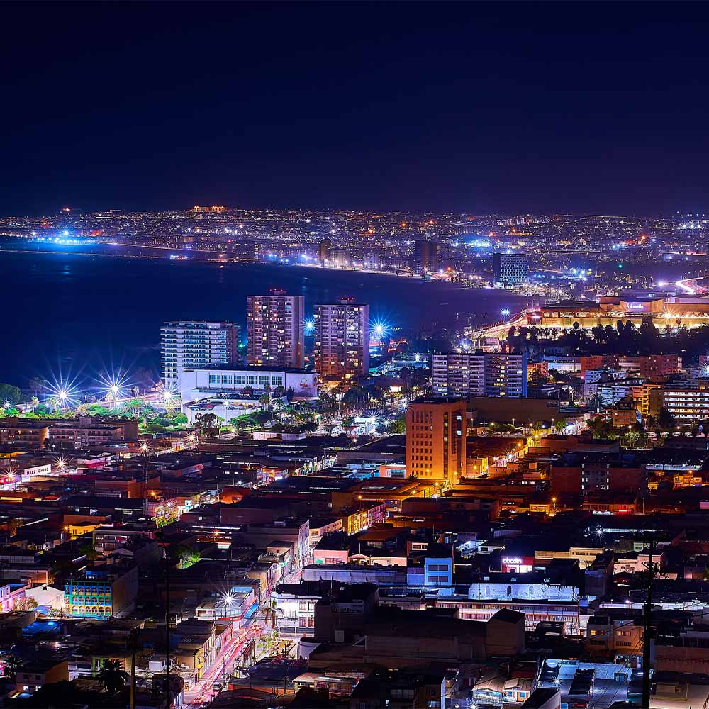 Nighttime view of a coastal city with illuminated buildings and streets seen from above