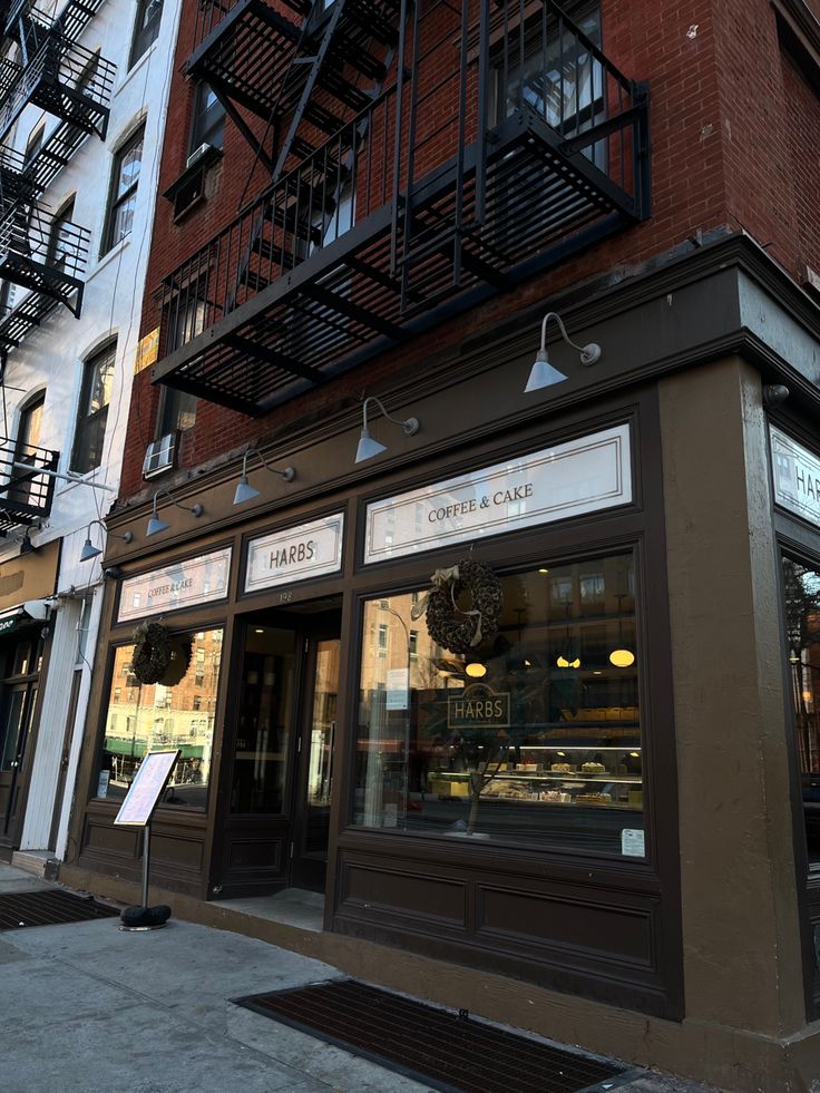 Street-level view of a coffee and cake café with dark wood exterior and fire escape in NYC