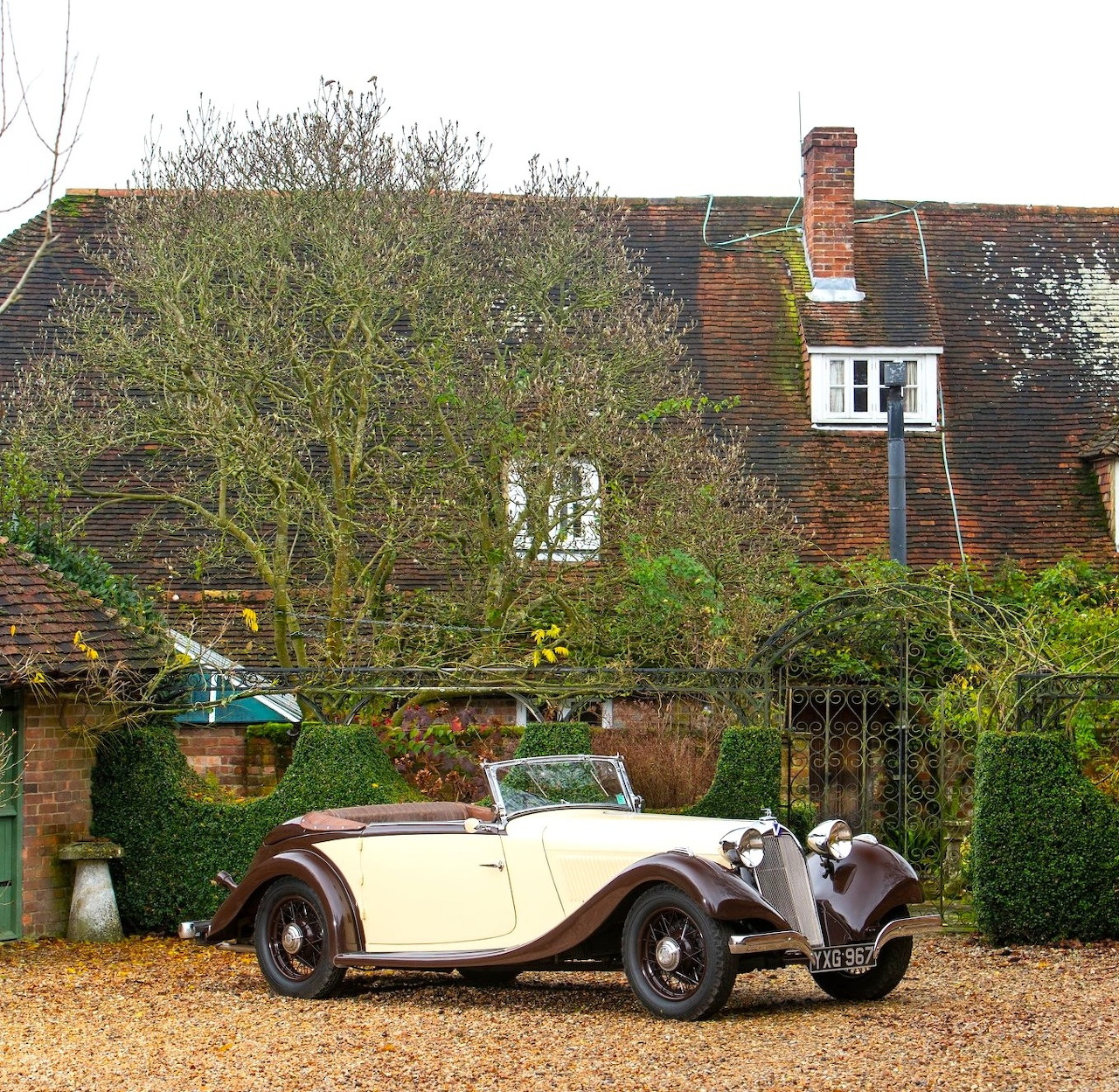 Vintage cream and brown convertible car parked on a gravel driveway before a brick house