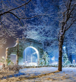 Illuminated stone archway in snowy park at night with blue lighting and frost-covered trees