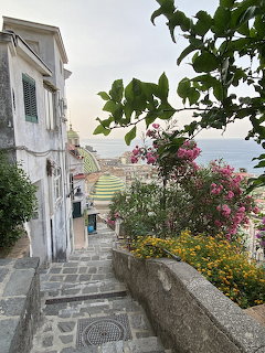 Stone steps leading down through a coastal Italian village with pink flowers and ocean view