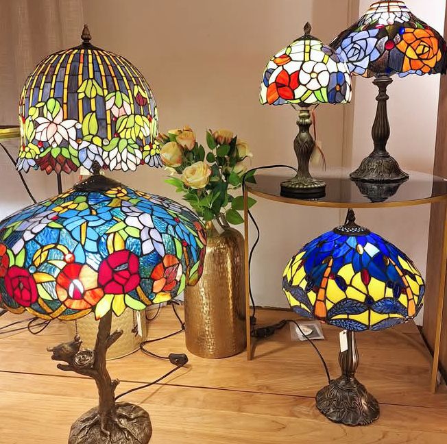 Five ornate stained glass lamps in various colors with floral designs on dark bronze bases