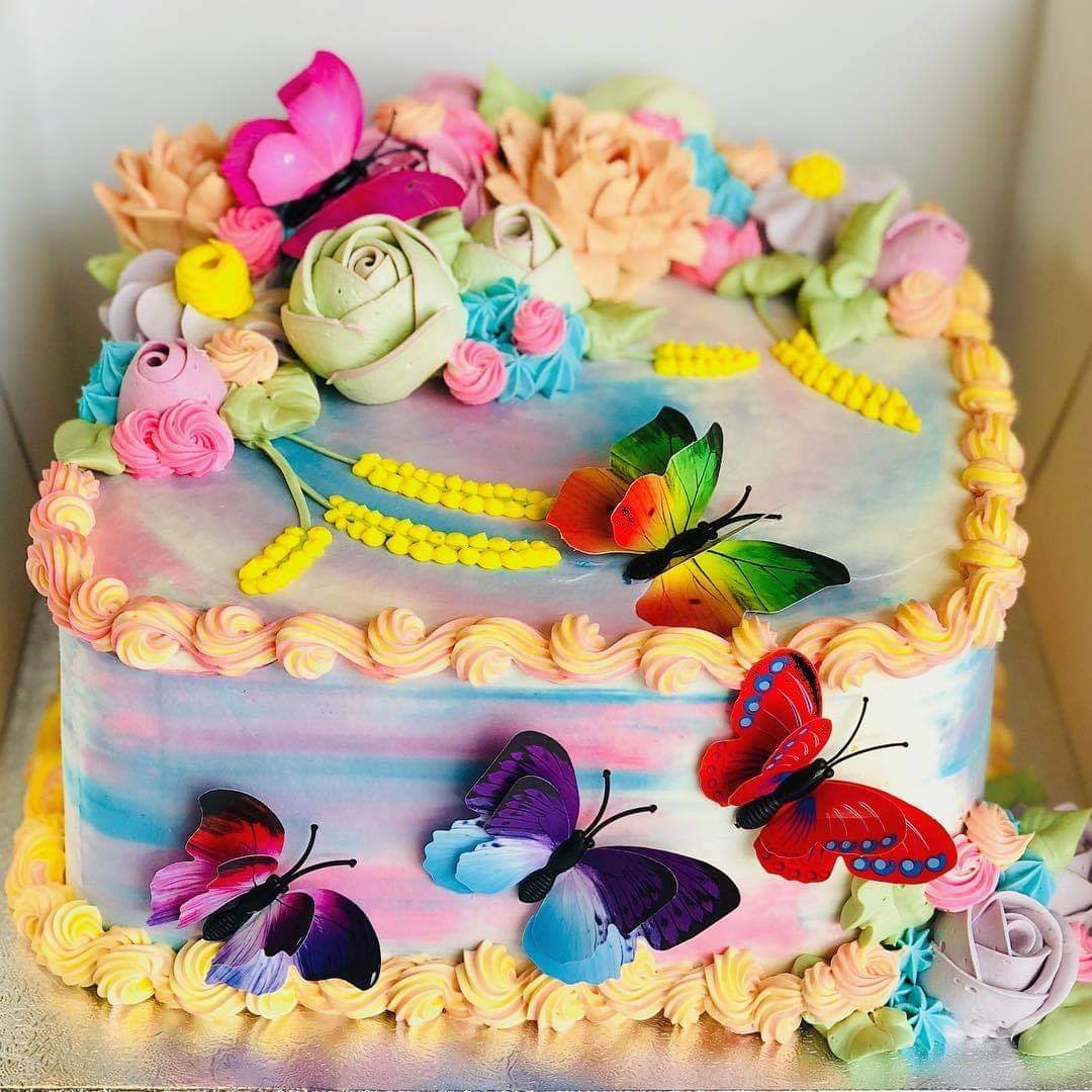 Decorated cake with rainbow layers, buttercream flowers, and colorful butterflies