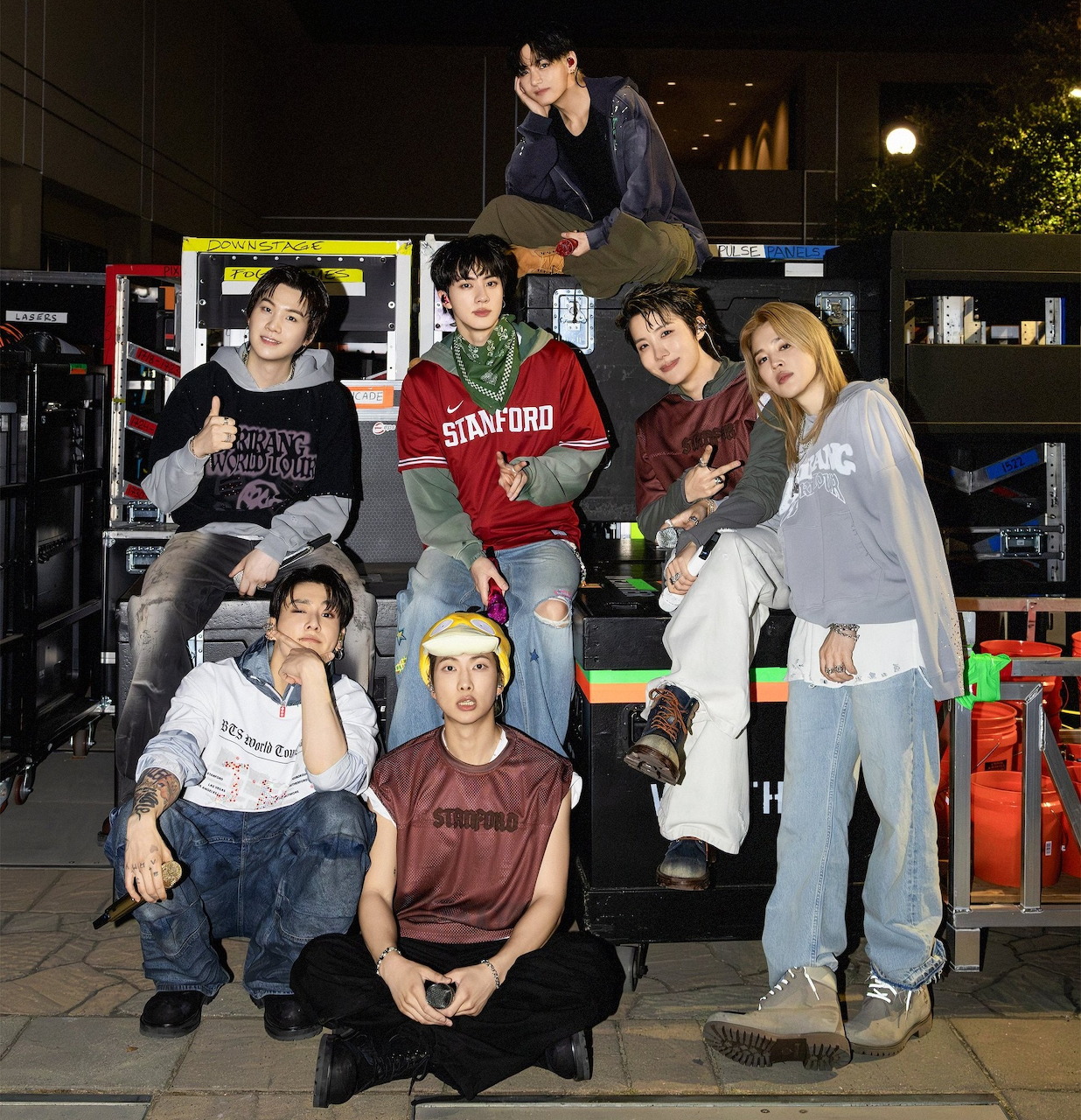 Seven young men in casual clothing posing together for a group photo at an arcade at night