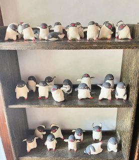 Ceramic penguin figurines arranged on three wooden shelves