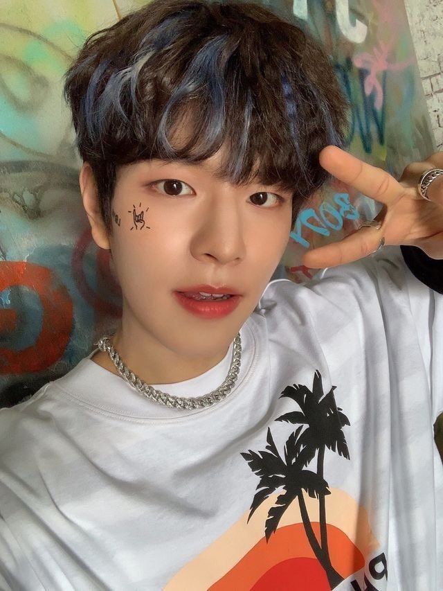 Portrait of young person with dark hair making peace sign, wearing white graphic t-shirt