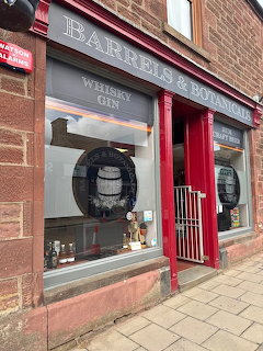 Front view of Barrels & Botanicals whiskey shop with large windows and a red entrance