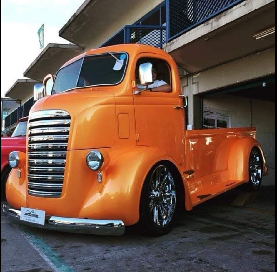 Bright orange vintage cab-over pickup truck parked beside a building