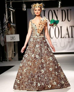 Model in a full-length brown chocolate evening gown with floral decorations on a fashion runway