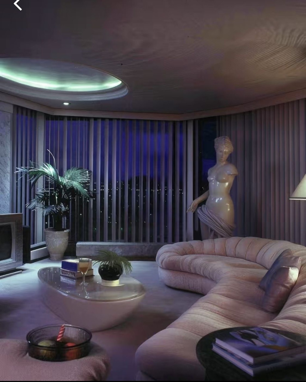 Modern living room with curved sofa, coffee table, potted palm, statue, and tall vertical blinds