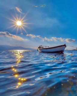 Small white boat on calm blue ocean with bright sunstar and clouds in the sky