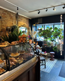 Cozy cafe interior with glass pastry display, brick walls, and lush green plants by a sunny window